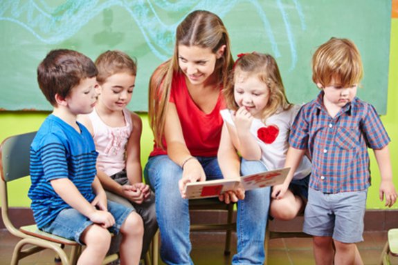 Glückliche Kinder mit Erzieher lesen gemeinsam ein Buch im Kindergarten