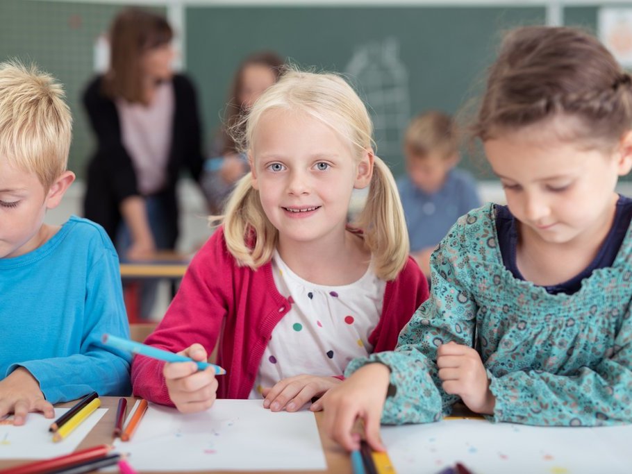 Zwei Mädchen und ein Junge im Grundschulalter vor Heften sitzend mit Stiften in der Hand